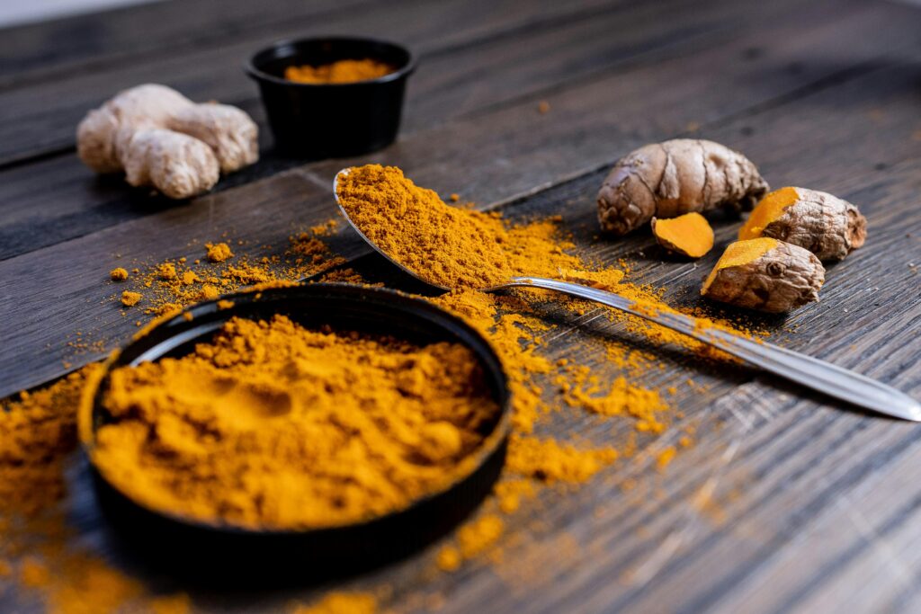 Pó de cúrcuma famoso entre alimentos para a Memória, vibrante em uma tigela preta e em uma colher de metal sobre uma mesa de madeira escura, acompanhado de raízes de cúrcuma frescas ao fundo.