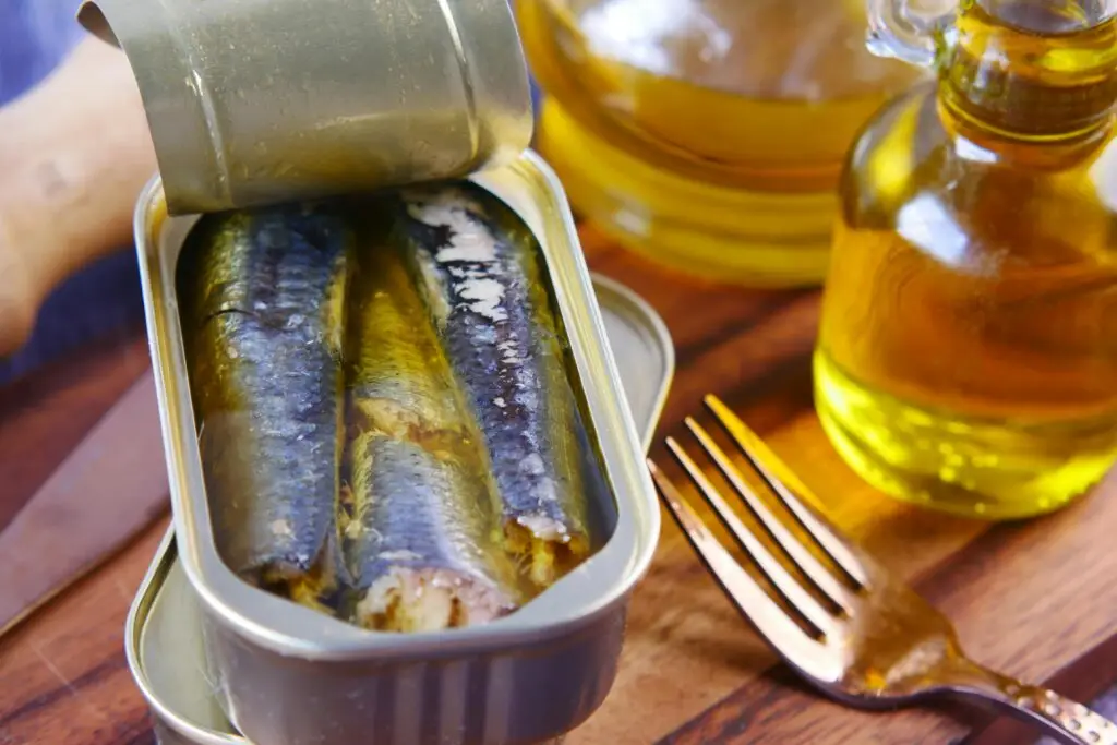 Lata de sardinha aberta em conserva com azeite de oliva ao lado de um garfo, ilustrando uma fonte acessível e natural de ômega-3.