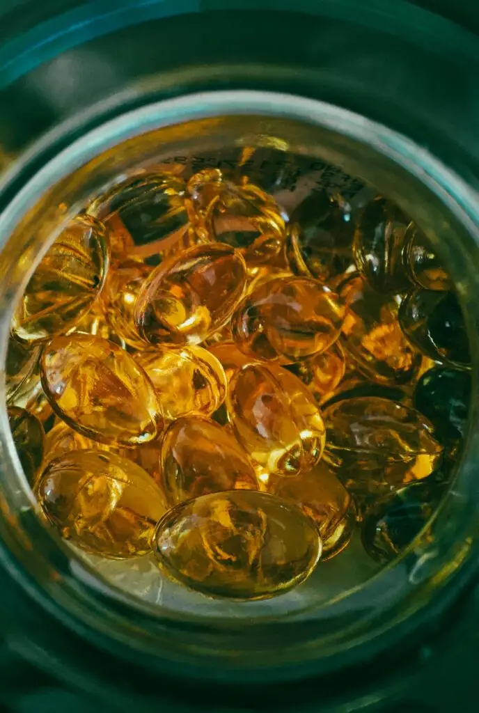 Visão superior de um frasco de vidro repleto de cápsulas de ômega-3 amareladas e brilhantes, destacando a suplementação como parte da rotina de saúde.