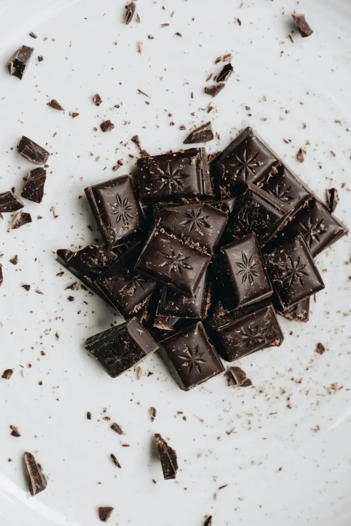 Pilha de quadrados de chocolate amargo e pedaços quebrados vistos de cima em um fundo branco, representando uma comida favorável para a memória.