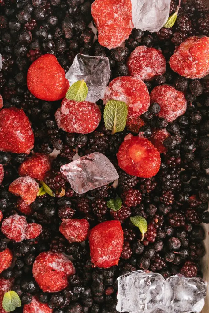 Mistura de frutas vermelhas congeladas, como morangos e amoras, com cubos de gelo e folhas de hortelã.