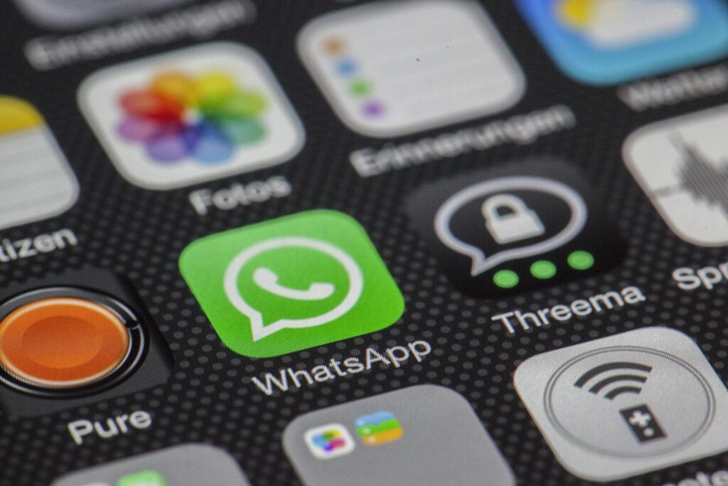 Close do ícone do aplicativo WhatsApp em destaque na tela inicial de um smartphone, cercado por outros ícones de aplicativos como Fotos, Threema e Ajustes sobre um fundo escuro texturizado. Foto serve introduzir as 5 funções escondidas no WhatsApp